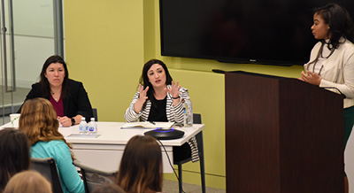 Employees in office. Two speaking behind a desk one standing behind a podium 