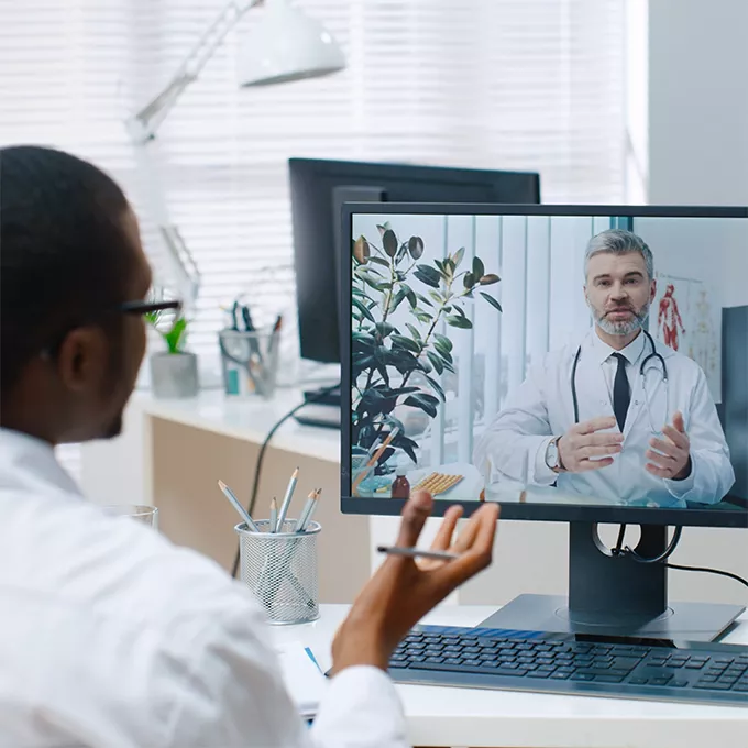 Two male physicians talking via video call on a desktop computer